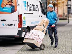 Ein Hermes Zusteller mit Paketen vor seinem Fahrzeug. Ein Hermes Zusteller mit Paketen vor seinem Fahrzeug.