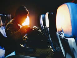 Mann sitzt im Flugzeug mit Rucksack auf dem Schoß